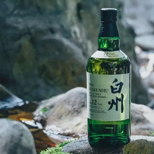 Green bottle of Hakushu whisky on rocks near a natural spring
