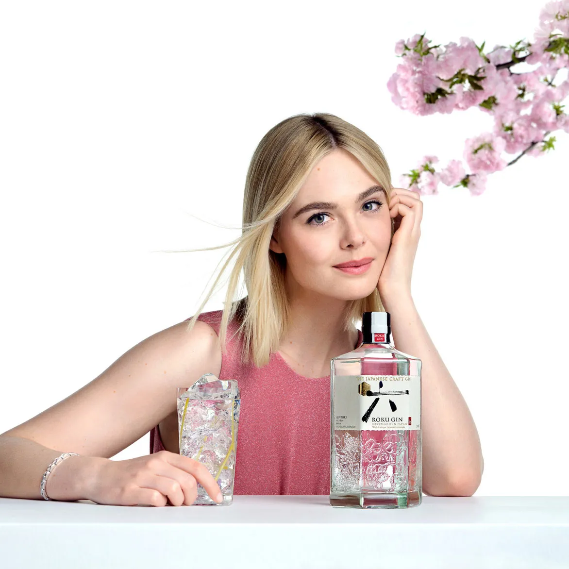 A women with a glass of roku gin and nearby roku gin bottle behind a blossom tree stem